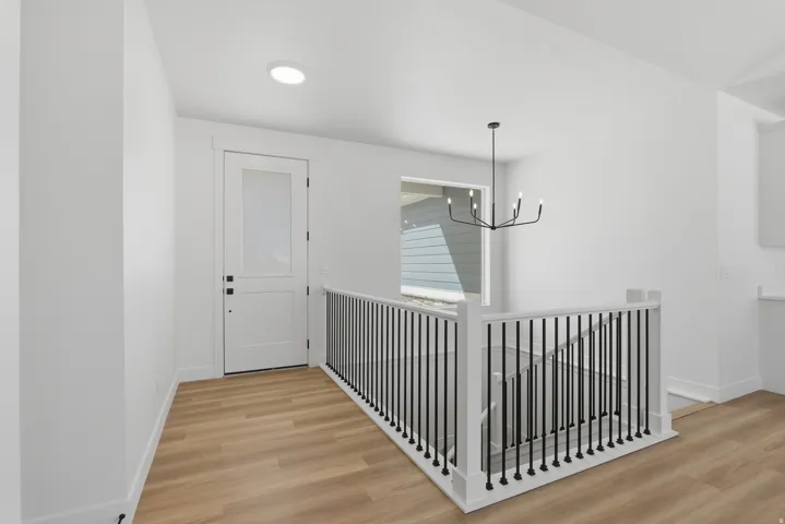White interior door with frosted glass panel, matte black hardware, wood-finish flooring, white walls, and a modern black chandelier
