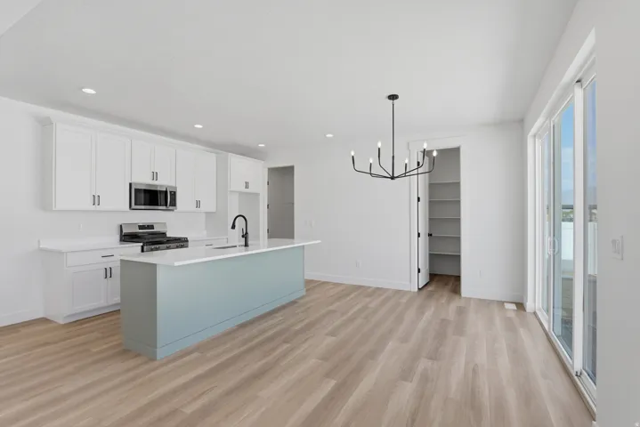 Contemporary kitchen featuring white cabinetry, a light blue island, white countertops, stainless steel appliances, and wood-finish flooring