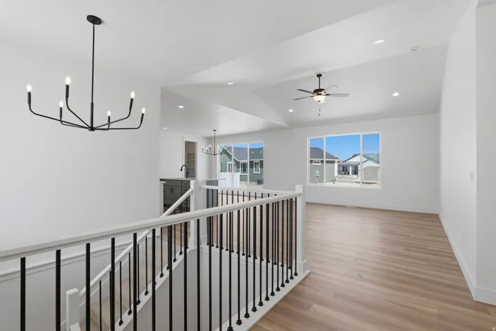 Modern black chandelier, vaulted ceiling, recessed lighting, wood-finish flooring, and large picture windows