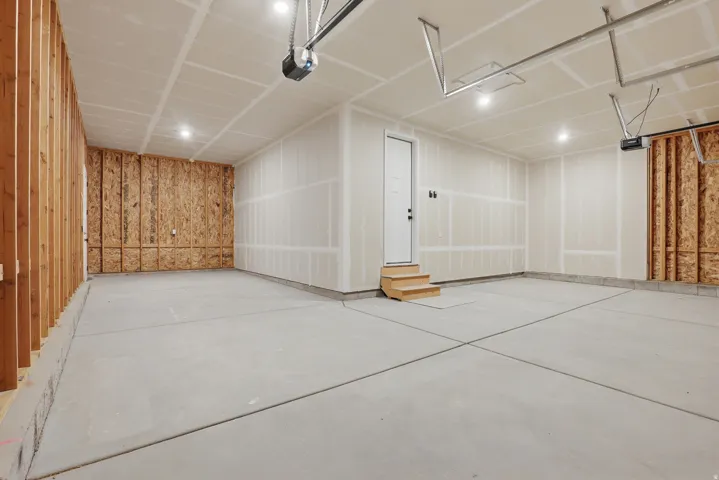 Spacious garage with concrete flooring, recessed lighting, exposed wood framing, and a utility door with wood steps
