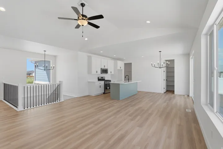 Vaulted ceiling with a ceiling fan, wood-finish flooring, white cabinetry, island with a basin sink, built-in shelving