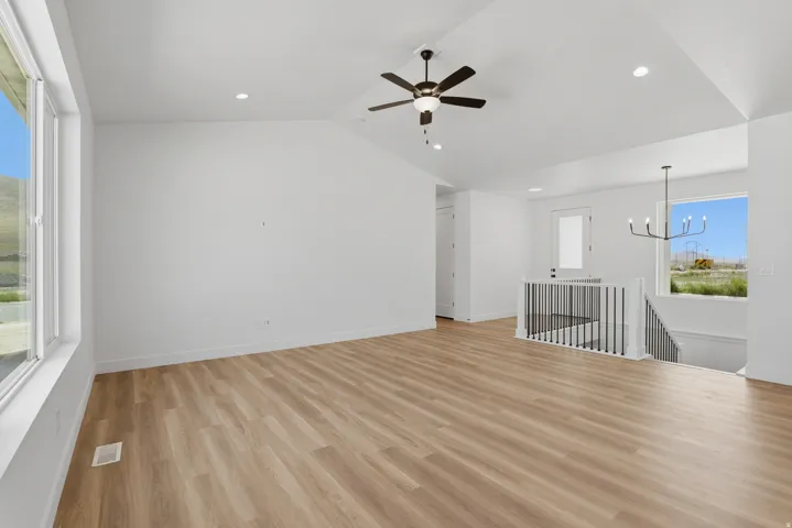 Vaulted ceilings, recessed lighting, wood-finish flooring, a ceiling fan, and a contemporary chandelier