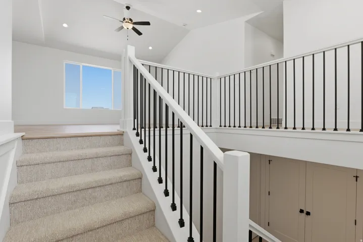 Carpeted staircase leading to a landing with wood-finish flooring, a white railing with black balusters, and a ceiling fan