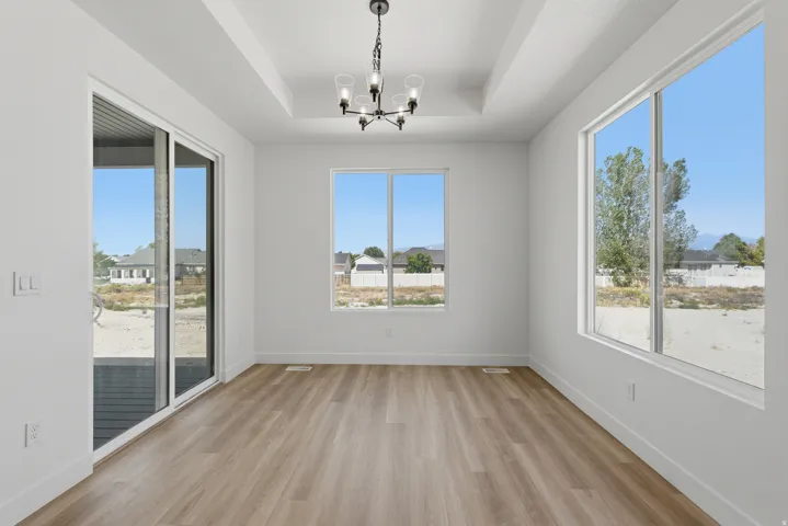 Recessed ceiling detail, wood-finish flooring, contemporary chandelier, multiple large windows, and a sliding glass door