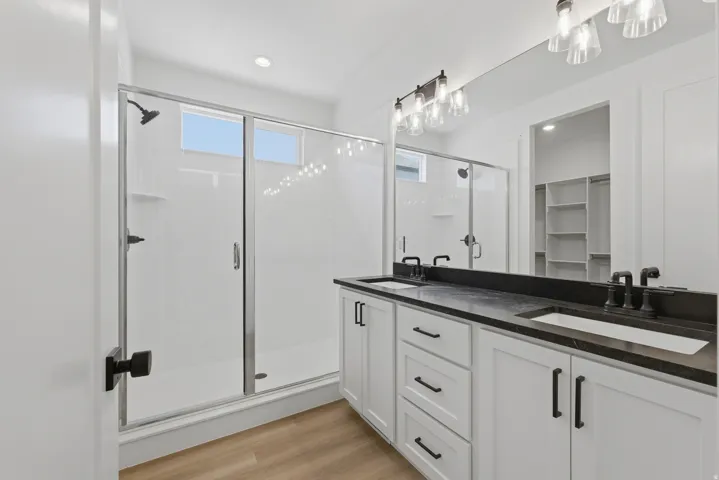Dual vanity with dark stone countertop, white shaker cabinetry, and integrated sinks