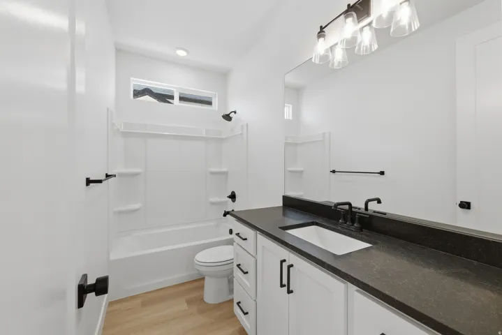 White vanity with dark countertop, large mirror, and wood-finish flooring