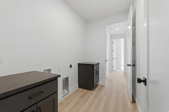 Laundry area with light wood-finish flooring, dark cabinetry, and white walls