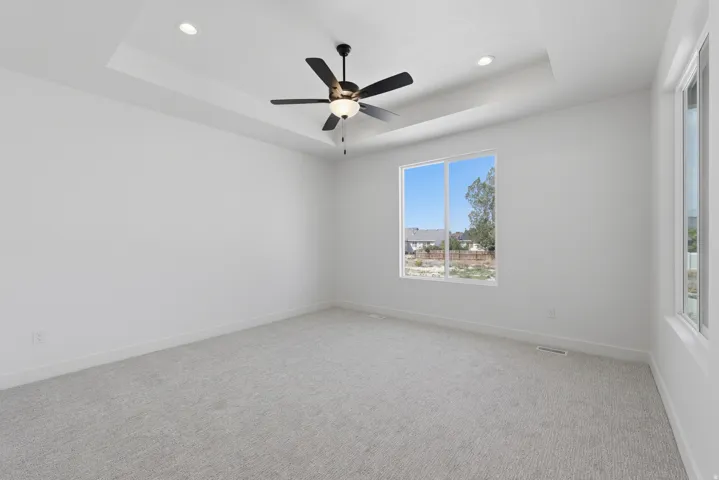 Recessed lighting, tray ceiling, ceiling fan, white walls, and light gray carpet