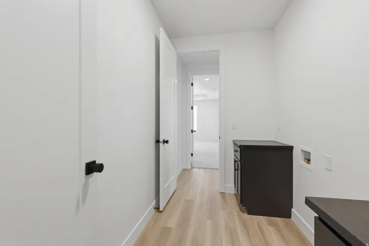 Light wood-finish flooring, white walls, and dark cabinetry with a coordinating dark countertop