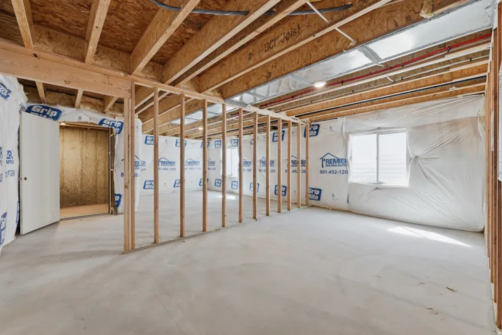Unfinished basement featuring exposed wood framing, concrete flooring, a single window, and a white interior door