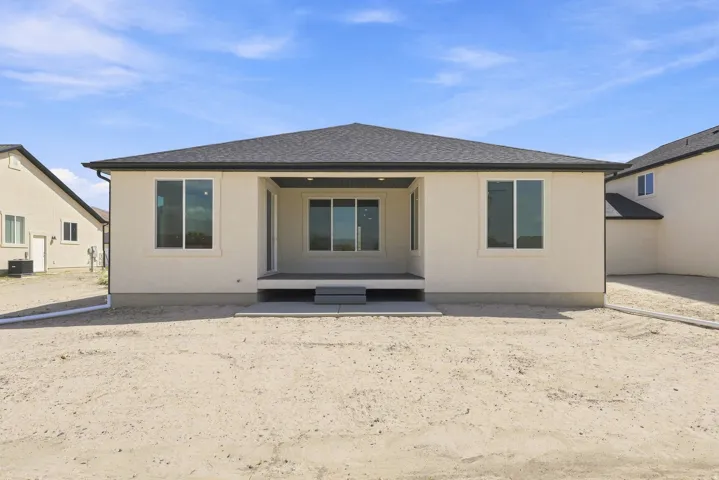 Rear exterior featuring a covered patio, multiple windows with white trim, and a dark shingle roof