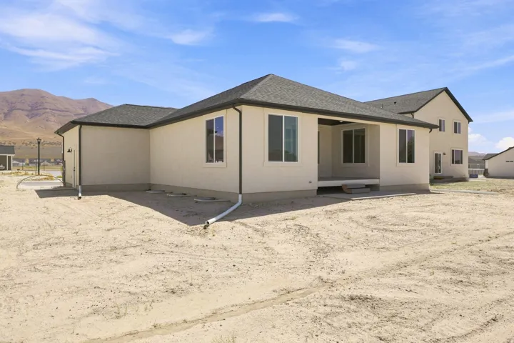 Single-story stucco exterior with a covered patio, multiple windows, and a dark shingle roof