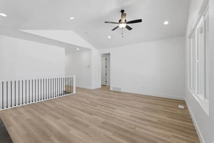 Vaulted ceilings with recessed lighting, wood-finish flooring, ceiling fan, and white railing with black balusters