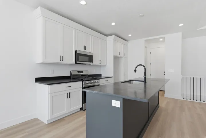 Modern kitchen featuring white cabinetry, dark countertops, stainless steel appliances, a center island with a sink, and wood-finish flooring