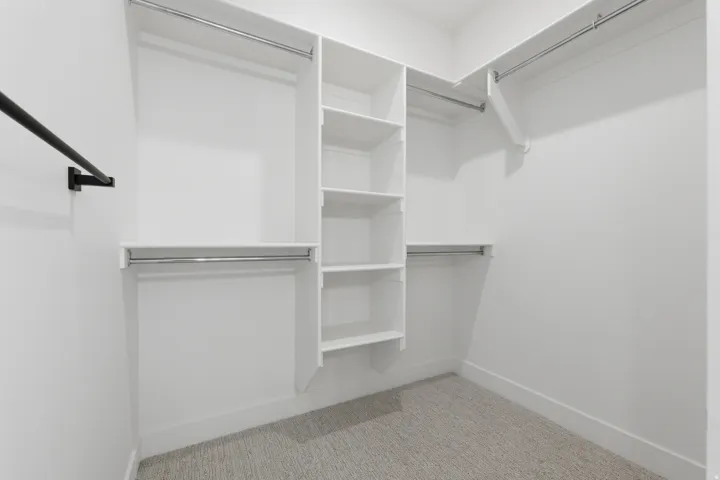 White built-in shelving, multiple hanging rods, and light-colored carpeted flooring