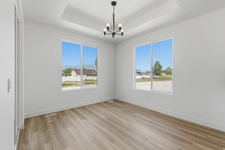 Recessed ceiling with a chandelier, wood-finish flooring, and white walls