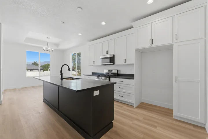 Open-concept kitchen with white shaker cabinetry, an island with an integrated sink, stainless steel appliances, and light wood-finish flooring