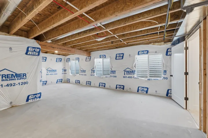 Unfinished lower level with exposed ceiling joists, three window wells, and concrete flooring
