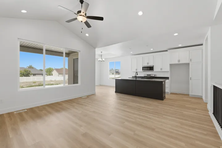 Vaulted ceilings, wood-finish flooring, white cabinetry, dark kitchen island, and black metal stair railing