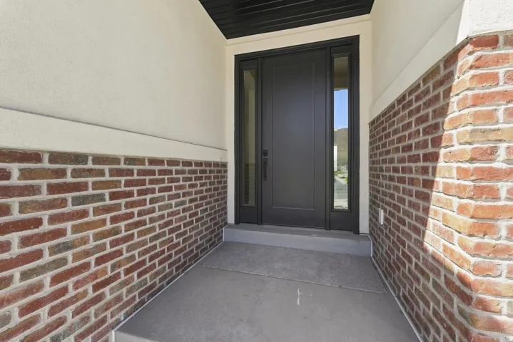Entryway featuring a dark paneled door with glass sidelights, textured stucco, and multi-toned brickwork