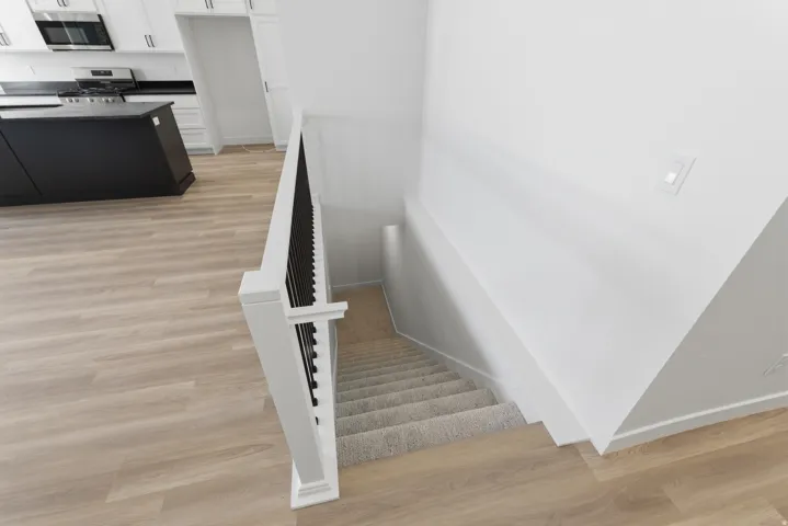 Wood-finish flooring, staircase with carpeted treads, white painted walls, and black balusters