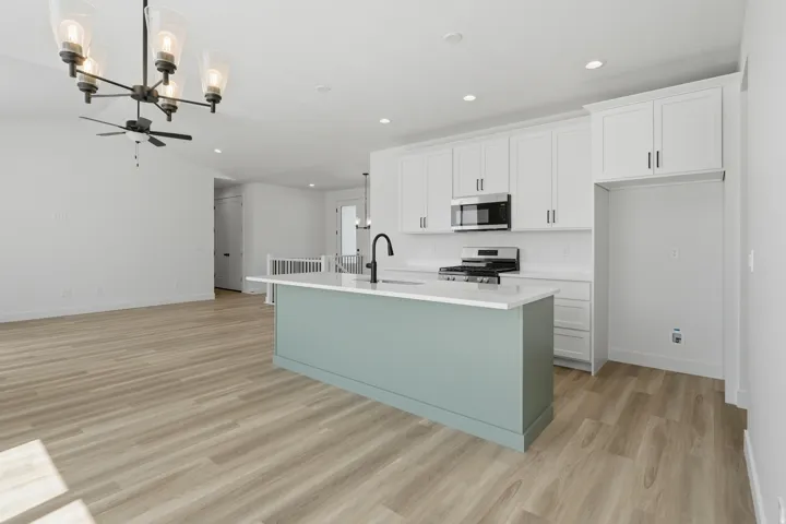 Open-concept kitchen with a light-colored island, white cabinetry, stainless steel appliances, and wood-finish flooring