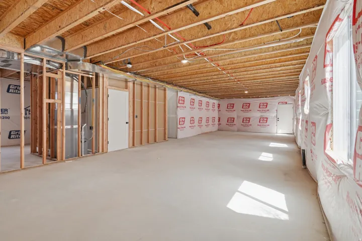 Unfinished basement featuring wood framing, exposed ceiling joists, concrete flooring, and multiple windows