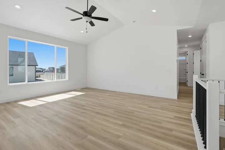 Vaulted ceiling with recessed lighting and a ceiling fan, wide plank wood-finish flooring, and a large multi-pane window