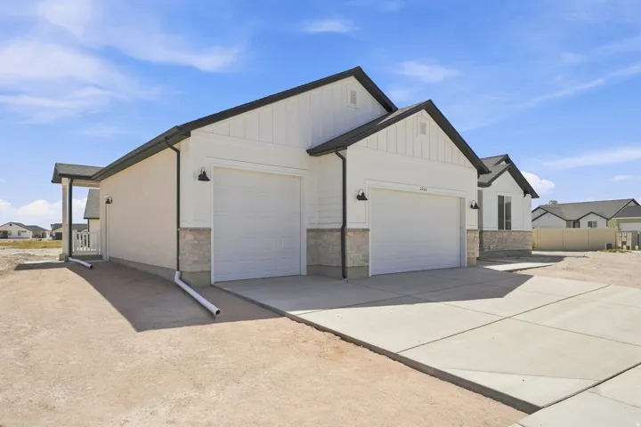 Contemporary exterior featuring white siding, stone veneer accents, a two-car garage, and a concrete driveway
