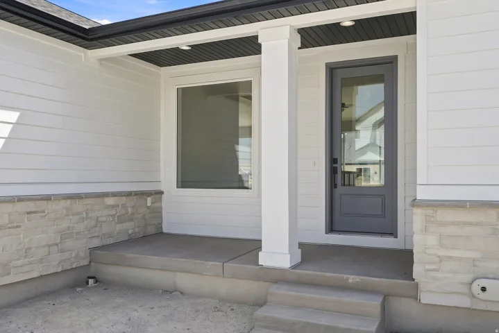 Entryway featuring a contemporary gray door with glass paneling, white siding, and a stone facade