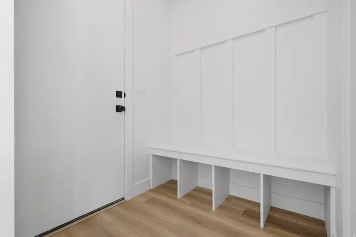 Built-in bench with cubby storage, board and batten wall detailing, wood-finish flooring, and a white door with matte black hardware