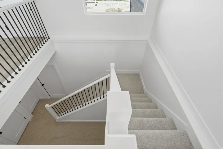 Staircase featuring carpeted treads, white newel posts, and black iron balusters