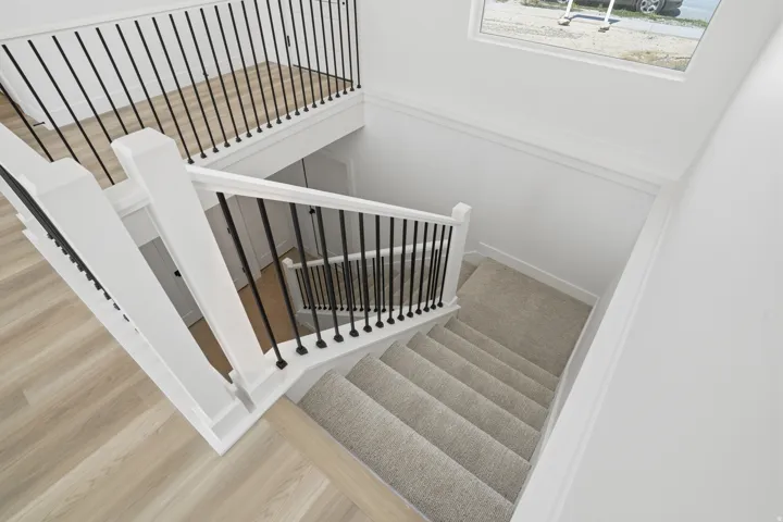 Staircase featuring carpeted treads, wood-finish flooring, white newel posts, and black metal balusters