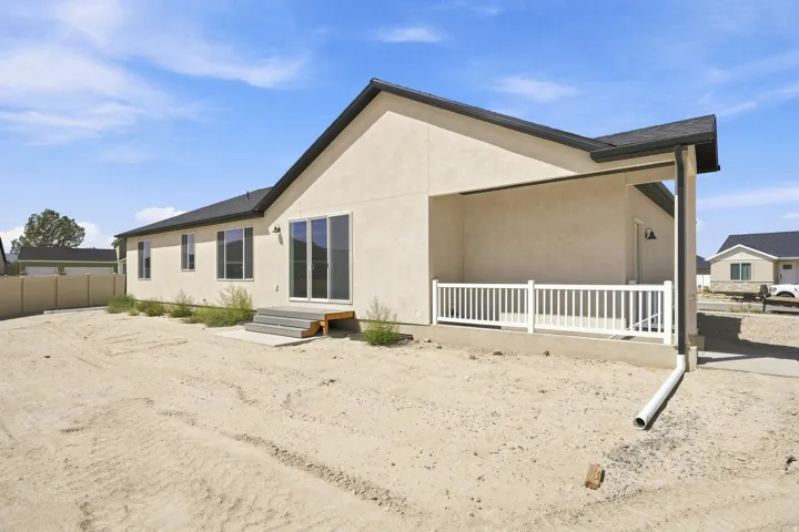 Beige stucco exterior with a dark shingle roof, featuring multiple windows, a covered patio with white railing, and a sliding glass door