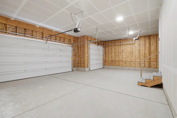 Spacious two-car garage with concrete flooring, two overhead garage doors, and unfinished wood framing