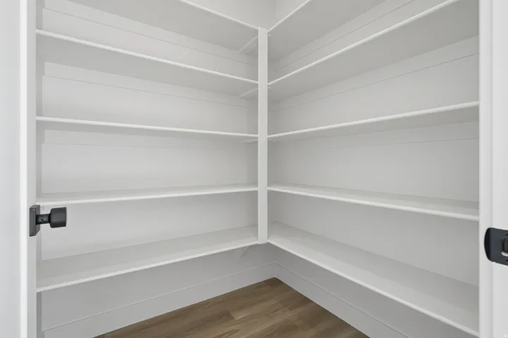 Walk-in pantry featuring expansive white shelving and wood-finish flooring
