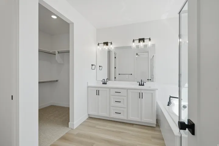 Dual sink vanity with white cabinetry, wood-finish flooring, built-in bathtub, and a separate glass-enclosed shower