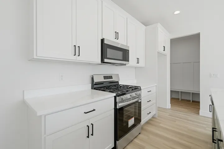 White shaker cabinetry, stainless steel range with overhead microwave, white countertops, and light wood-finish flooring