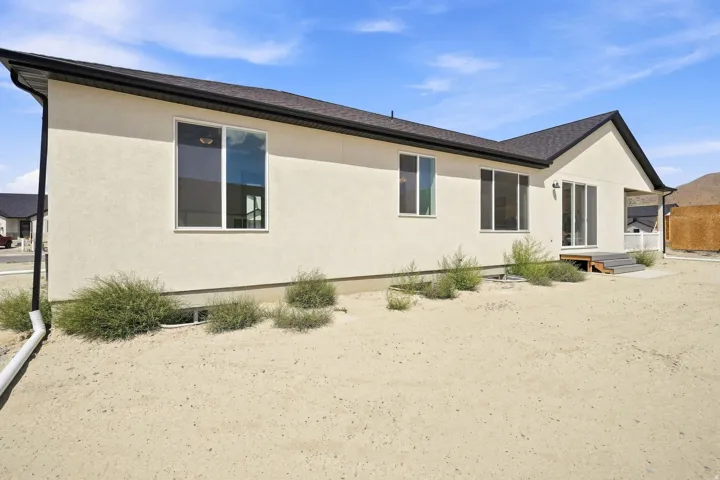 Stucco exterior with multiple large windows, dark shingle roof, and a rear patio with sliding glass doors
