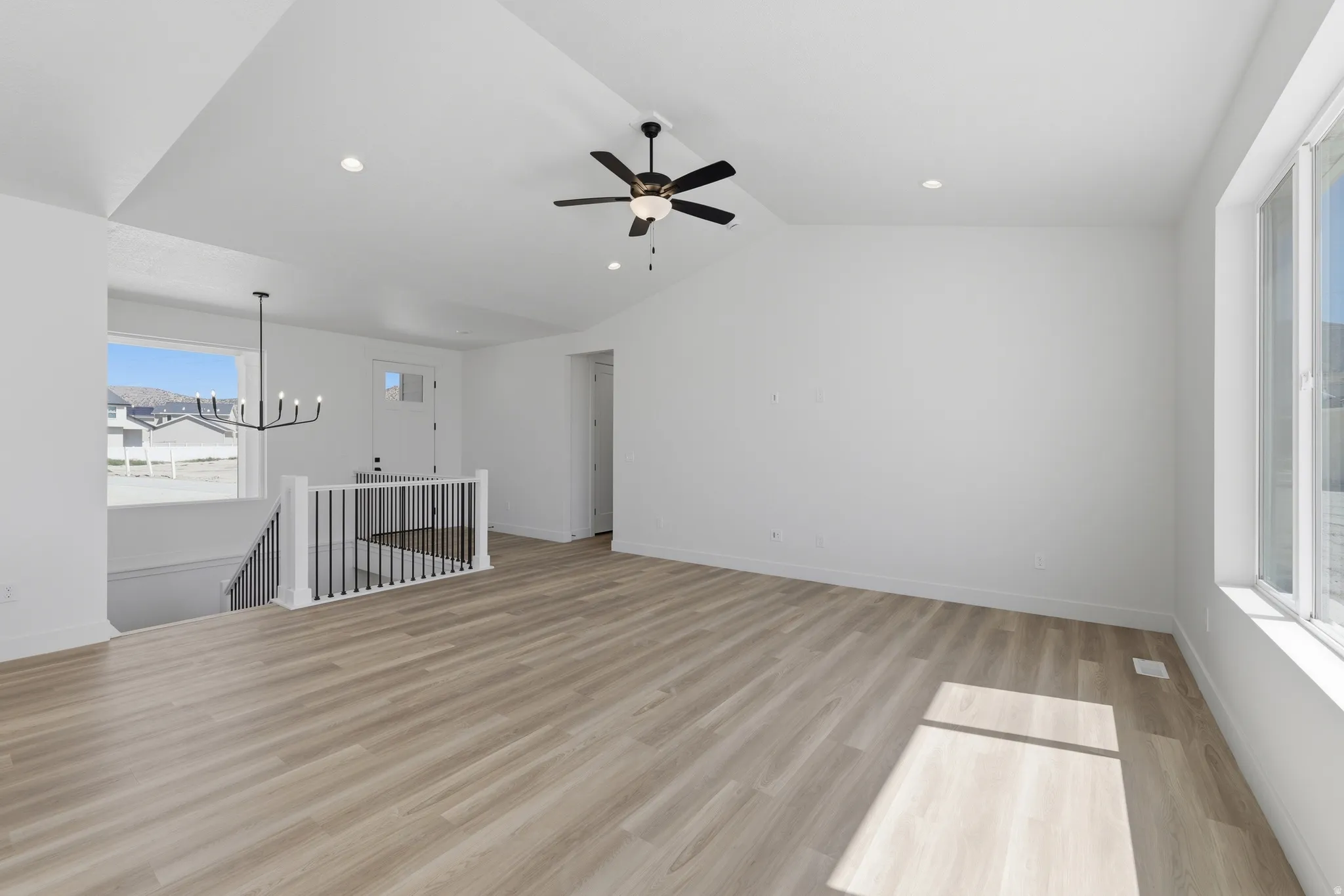 Vaulted ceiling with recessed lighting, wood-finish flooring, ceiling fan with integrated light, and large windows