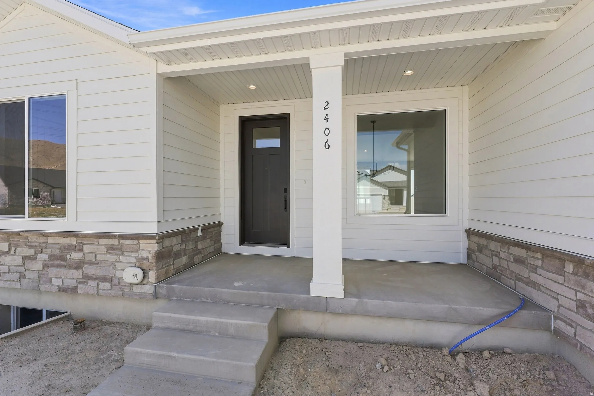 White horizontal siding exterior with stone veneer accents, an inviting covered front entry, recessed lighting, and a dark-paneled door with an integrated window