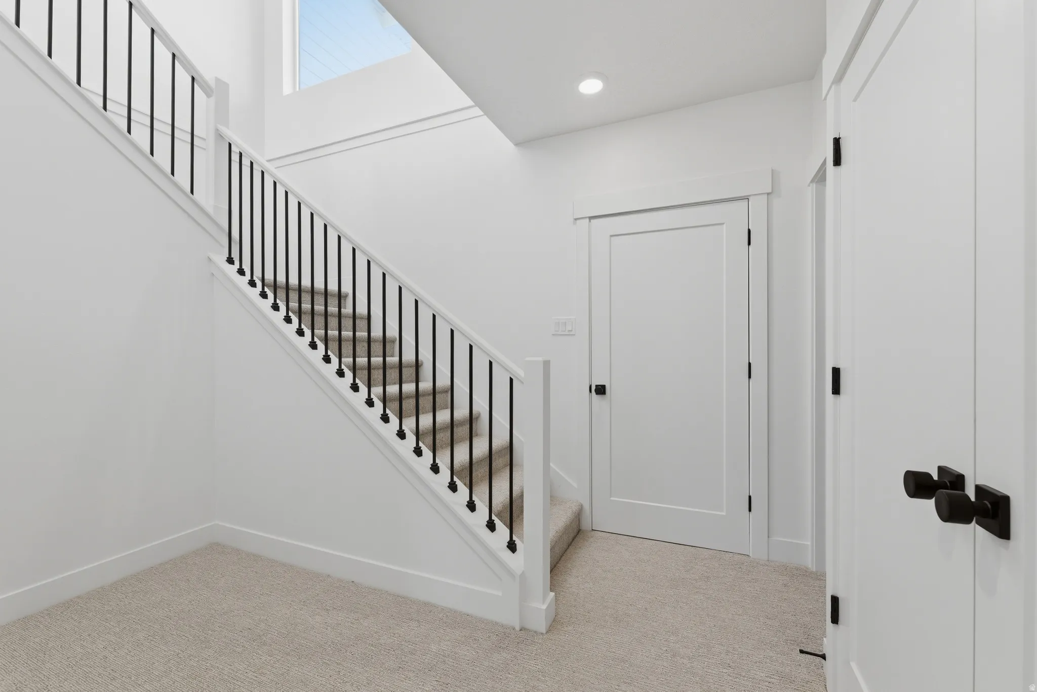 Staircase with black balusters and carpeted treads, white interior doors with black hardware, and recessed ceiling lighting