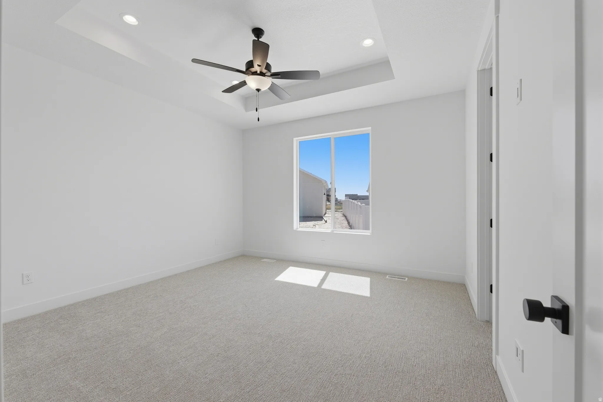 Recessed ceiling lighting, tray ceiling, ceiling fan, carpet flooring, and a large window