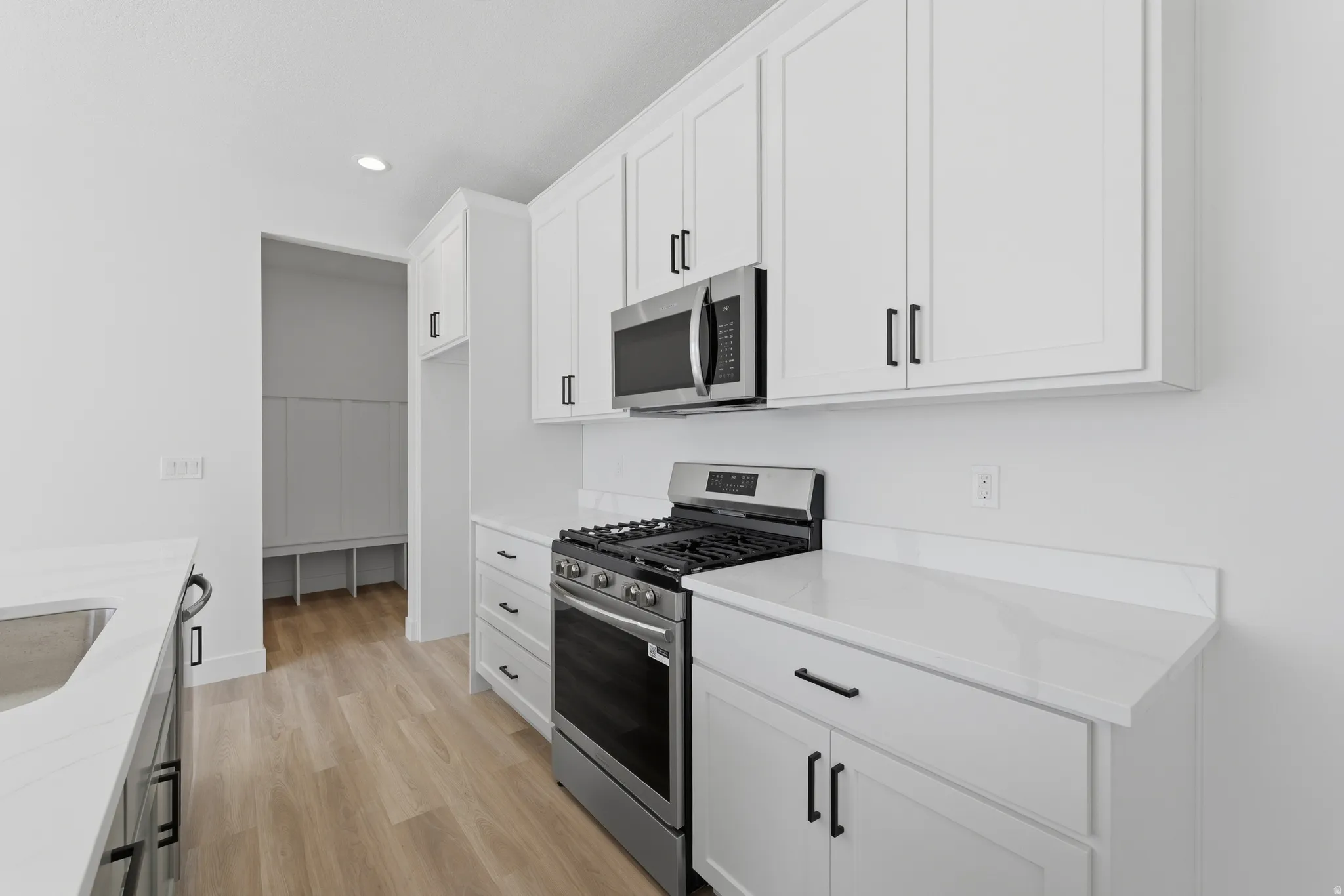 White shaker cabinetry with matte black hardware, stainless steel gas range, built-in microwave, white countertops, and wood-finish flooring