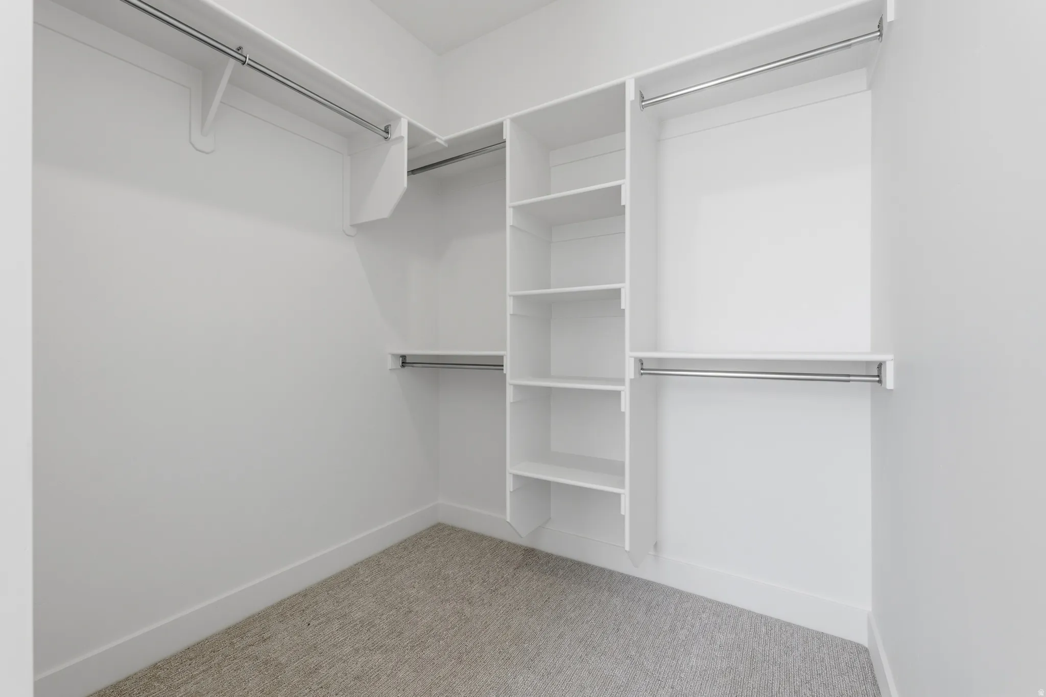Walk-in closet with built-in shelving, multiple hanging rods, and neutral-toned carpeting