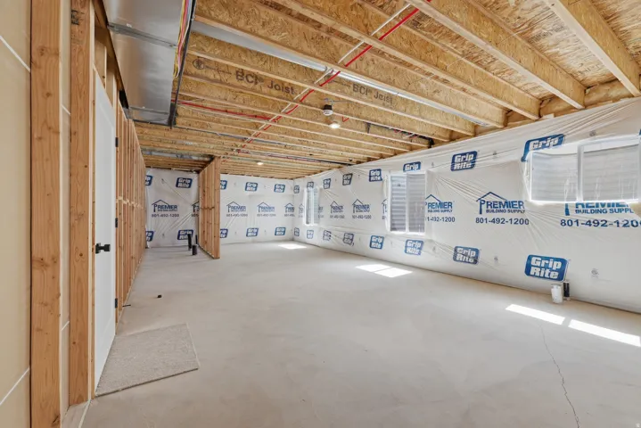 Unfinished space featuring concrete flooring, exposed wood joists, framed interior walls, and multiple windows