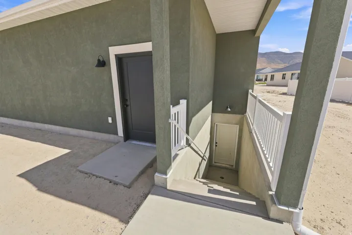 Stucco exterior with a covered entry, exterior lighting, and a separate basement entry with white railings