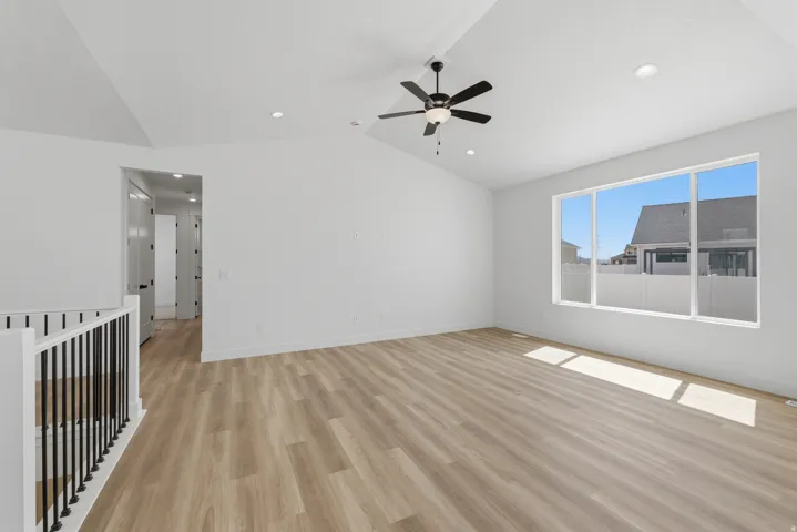 Vaulted ceiling with a ceiling fan, recessed lighting, wood-finish flooring, and a large window