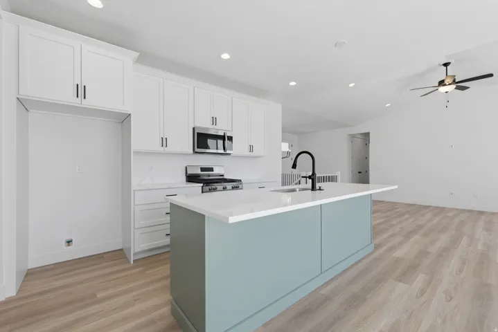 Modern kitchen featuring white shaker cabinetry, stainless steel appliances, a center island with a sink and matte black faucet, and wood-finish flooring