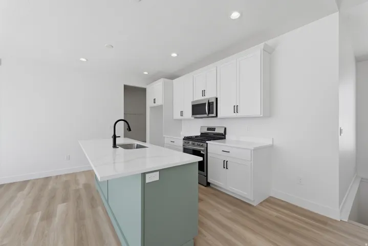 Kitchen featuring a central island with an integrated sink, white cabinetry, stainless steel appliances, and light wood-finish flooring